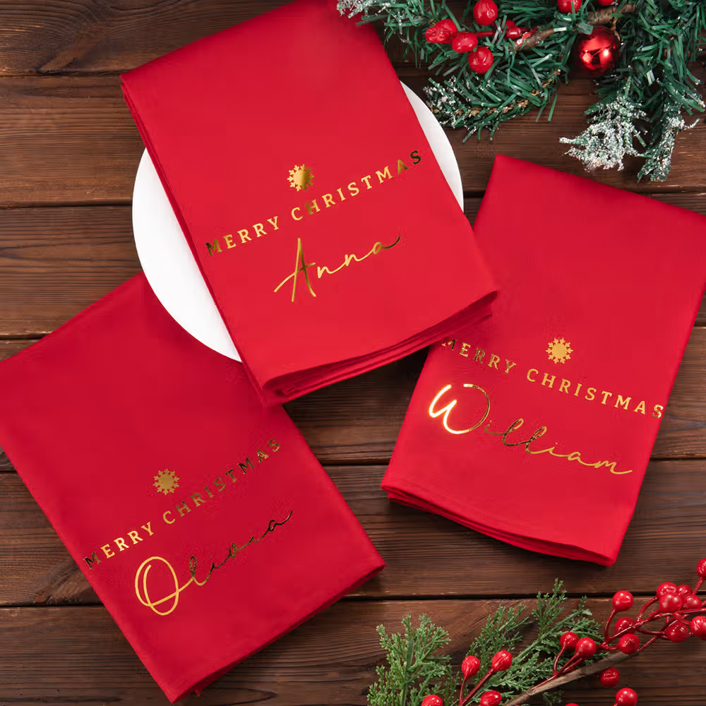 Three plates have three reusable Merry Christmas cotton napkins with gold names